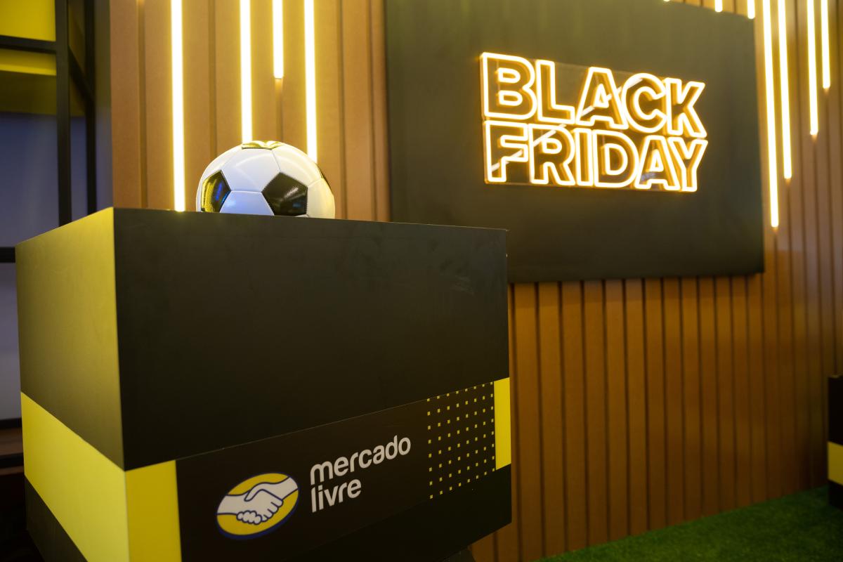 Caixa com o logo do Mercado Livre, com uma bola em cima. Na parte de trás, uma parede de madeira e um  letreiro em neon escrito "Black Friday"