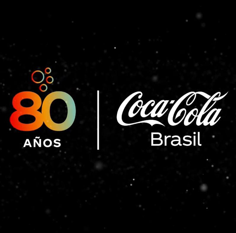 Imagem com fundo preto, escrito 80 anos em gradiente de vermelho, laranja, amarelo e azul claro, e logo da empresa coca-cola brasil em branco